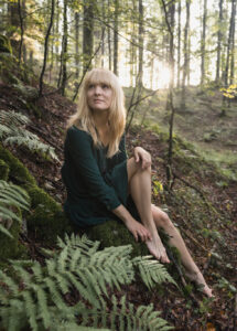 Kaja Gulic, tutor, sitting among ferns in a sunlit forest